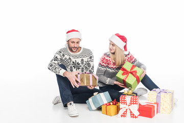 couple in sweaters and santa claus hats with wrapped presents sitting on floor isolated on white