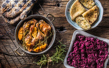Roasted duck legs in pan with oranges herbs red cabbage and potato pankaces