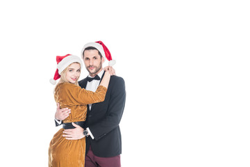 portrait of fashionable couple in santa claus hats hugging isolated on white