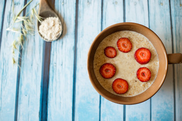 oatmeal porridge in ceramic bowl with fresh ripe berries over blue wooden background