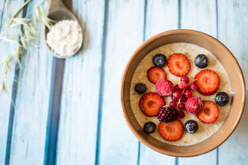 oatmeal porridge in ceramic bowl with fresh ripe berries over blue wooden background