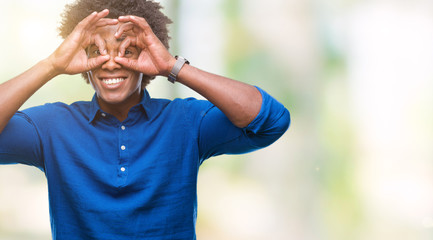 Afro american man over isolated background doing ok gesture like binoculars sticking tongue out, eyes looking through fingers. Crazy expression.