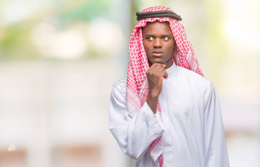 Young arabic african man wearing traditional keffiyeh over isolated background with hand on chin thinking about question, pensive expression. Smiling with thoughtful face. Doubt concept.