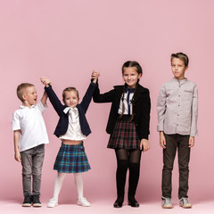 Cute smiling happy stylish children on pink background. Beautiful stylish teen girls and boy standing together and posing at studio. Classic style. Kids fashion and emotions concept.