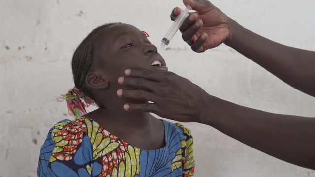 African girl gets an oral vaccine with a syringe. 4K RAW clip, please modify and edit (color grade, stabilize, etc.) in postproduction.