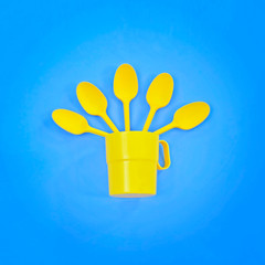 A yellow plastic mug and spoons lay in it on a bright blue background. The concept of a holiday, a picnic.