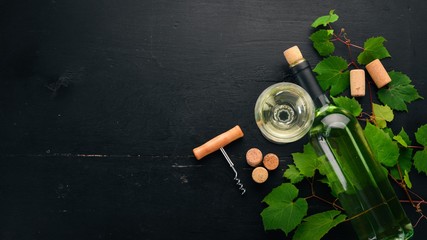 White wine in a bottle with a glass and grapes. On a black wooden background. Free space for text. Top view.
