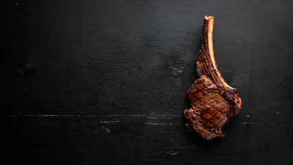 Steak on the bone. tomahawk steak On a black wooden background. Top view. Free copy space.