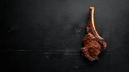 Poster Steak on the bone. tomahawk steak On a black wooden background. Top view. Free copy space. © Yaruniv-Studio