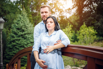 Romantic portrait of young smiling happy couple of lovely future parents during sunset on nature apple tree background in the city park. Pregnancy pregnant future mother photoshoot.