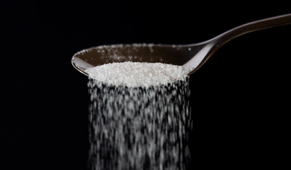 Obraz na płótnie Canvas Close up of spoon pouring granulated refine white sugar