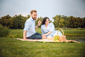 Happy joyful young family husband and his pregnant wife having fun together outdoors, at picnic in summer park, countryside.