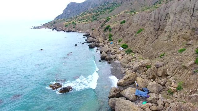 Aero view drone shot over green mountains hills beach, tourist tents on beach ocean and beach Cape Point Megan Crimea, rocks by sea. Cape Town Flying Over blue lagune to Ocean Drone Footage Black sea.