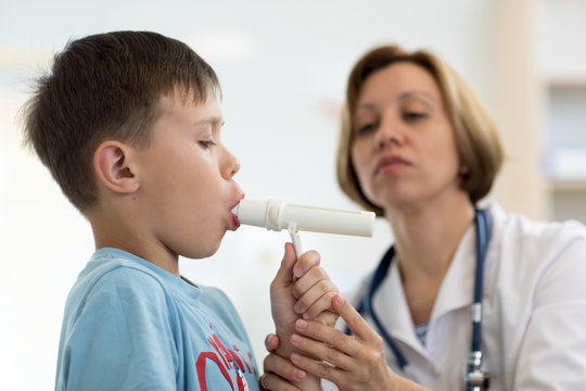Cute child boy blowing to peak metr medical device. Doctor examining kid's lungs