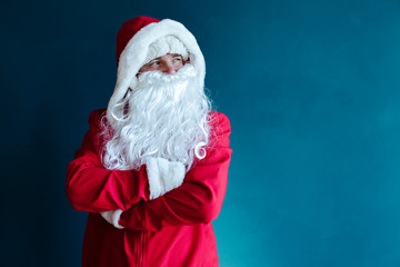 Serious Santa Claus  in festive Christmas outfit on the blue wall background
