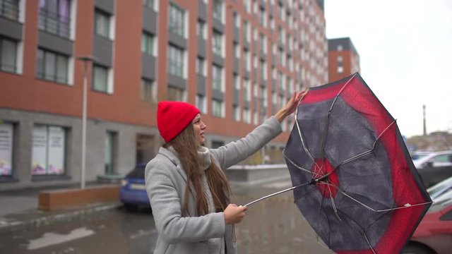 Young female woman, girl with umbrella standing outdoors. The gust of wind pulls umbrella out of hand. umbrella girl. Bad miserable weather, high wind and rain storm. Flu, cold, disease, health, 4 K