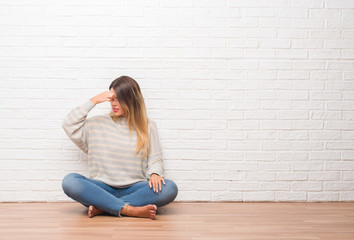 Young adult woman sitting on the floor over white brick wall at home tired rubbing nose and eyes feeling fatigue and headache. Stress and frustration concept.