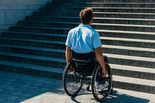 back view of man using wheelchair on street and looking at stairs without ramp
