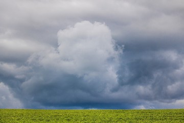 Minimalism photo of a dramatic cloud over a green field.