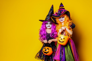 Two Beautiful girls in a witch costumes and hats on a yellow background scaring and making faces....