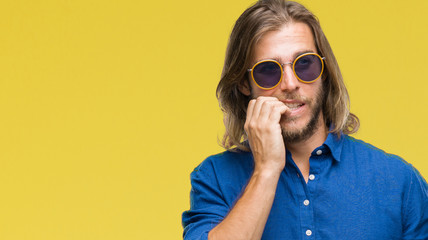 Young handsome man with long hair wearing sunglasses over isolated background looking stressed and nervous with hands on mouth biting nails. Anxiety problem.