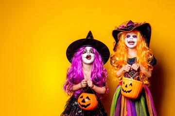 Two Beautiful girls in a witch costumes and hats on a yellow background scaring and making faces....