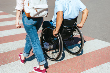 cropped image of disabled boyfriend in wheelchair and girlfriend crossing crosswalk in city