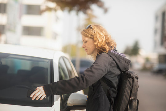 Woman standing by a car opening the door with her mobile phone