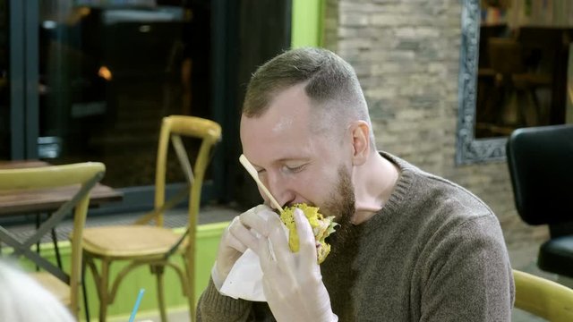 Burger. Handsome young man eating fast food, tasty hamburger in a restaurant. 4K