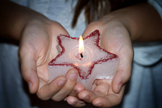 Child's hands holding candle christmas star in night sign of hope concept
