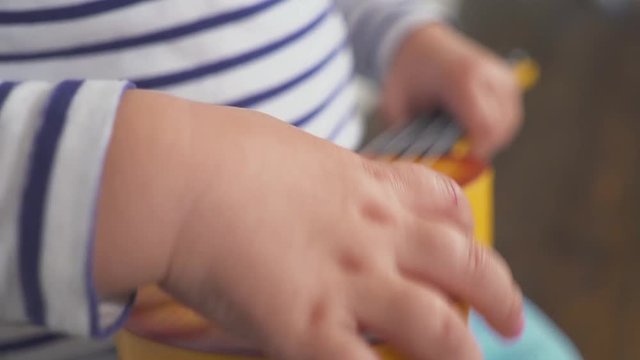happy one year old boy plays his guitar or ukulele and sings songs, sitting in the wooden room.