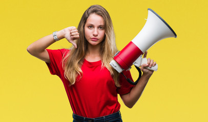 Young beautiful blonde woman yelling through megaphone over isolated background with angry face, negative sign showing dislike with thumbs down, rejection concept
