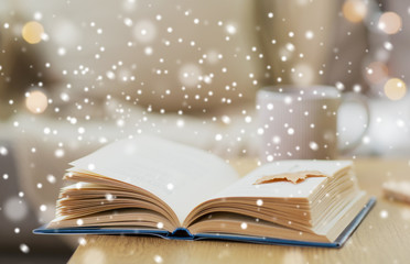 winter, literature and reading concept - open book with autumn leaf on wooden table at home over...