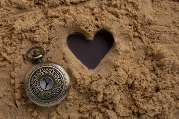 Fototapeta na wymiar Retro style watch beside a heart shape on sand