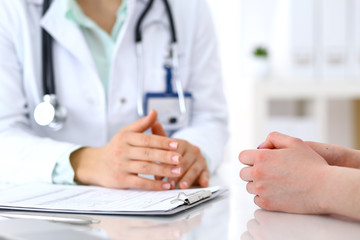 Doctor and patient talking while sitting at the desk in hospital office, close-up of human hands. Medicine and health care concept