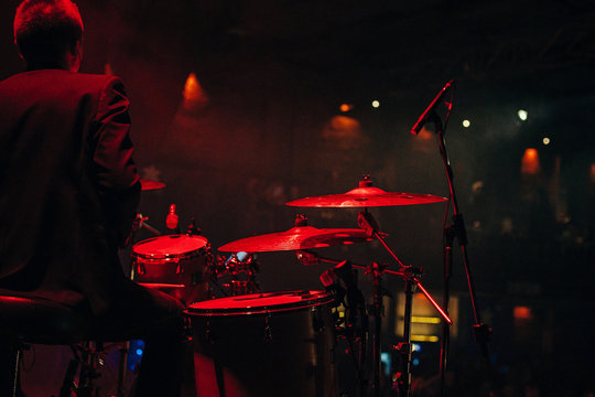 Drummer playing drum set at concert on stage. Music show. Bright scene lighting in club,drum sticks in hands