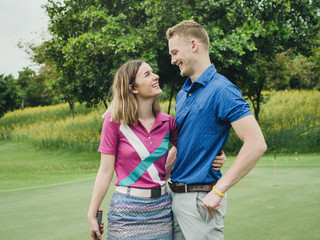 Happy golfer couple hugging together at green field outdoor.