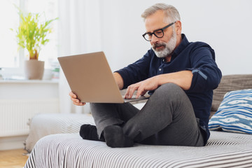 Man sitting cross-legged on a bed with his laptop