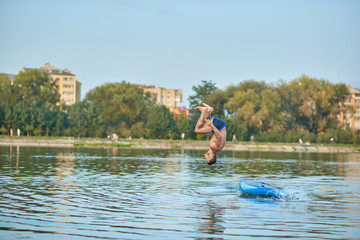 Fototapeta na wymiar Man training on paddle board, jumping into water head down at city lake.
