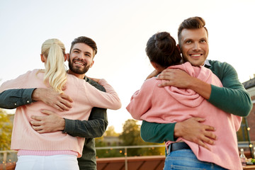 leisure and people concept - happy couples or friends hugging at on rooftop party