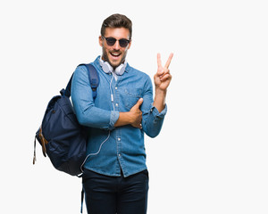 Young handsome tourist man wearing headphones and backpack over isolated background smiling with happy face winking at the camera doing victory sign. Number two.