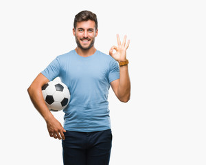 Fototapeta Young handsome man holding soccer football ball over isolated background doing ok sign with fingers, excellent symbol obraz