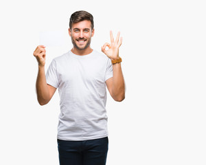 Young handsome man holding blank card over isolated background doing ok sign with fingers, excellent symbol