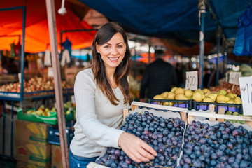 Portrait of a young woman buying grapes at street market. Looking at camera.