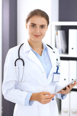 Doctor woman in clinic office. Female physician at work using digital tablet  while standing straight at hospital. Medicine and healthcare concept