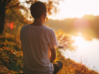 A young man sits with his back to the camera and enjoys the autumn sunset. Copy space