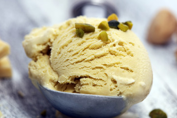 Pistachio ice cream scoop with chopped nuts and white chocolate on a rustic background.