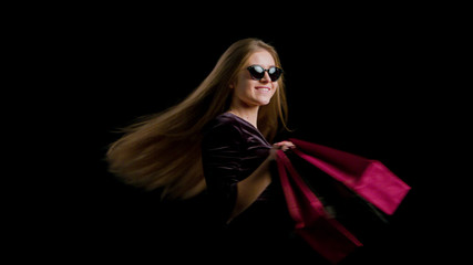 Obraz na płótnie Canvas Woman in cool sunglasses and black dress, holding black shopping bag isolated on dark background in black friday holiday or christmas