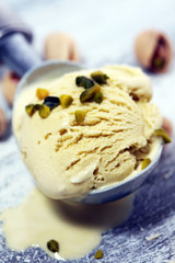 Pistachio ice cream scoop with chopped nuts and white chocolate on a rustic background.