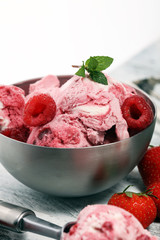 Strawberry and raspberry ice cream scoop with chopped nuts and white chocolate on a rustic background